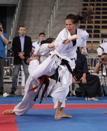 Anna Lewandowska in a white karategi with a black belt during a karate competition, mid-technique against an opponent