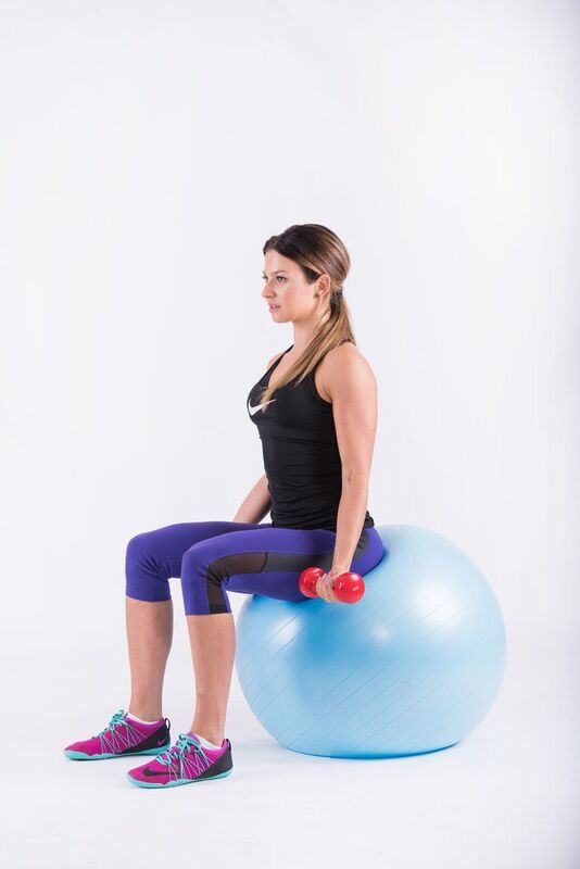 Sitting on the ball with dumbbells held down at the sides of the body