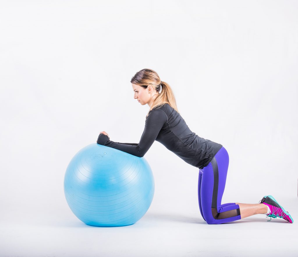 Kneeling behind an exercise ball with the arms resting on top, the starting position