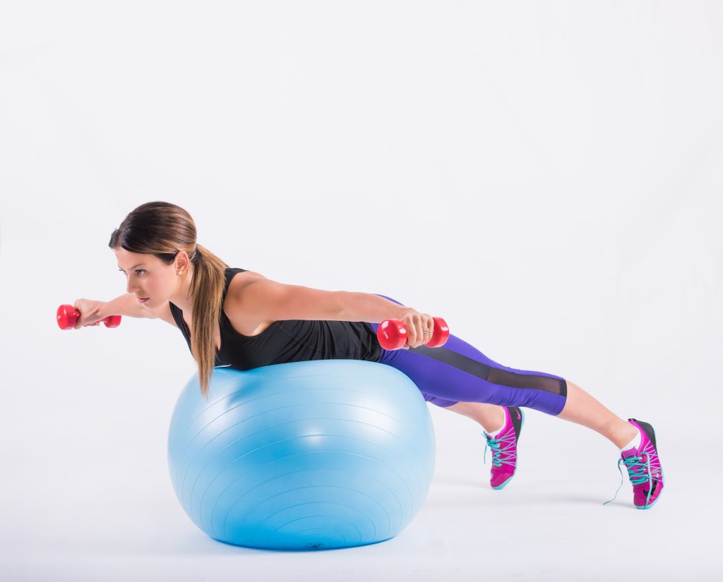 Lying face down over the ball with dumbbells held out to the sides, elbows bent