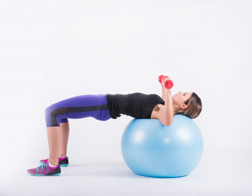 Lying with the shoulder blades on the ball and dumbbells held at chest level