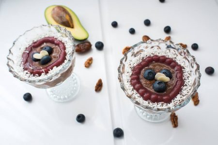 Two glass cups of chocolate zucchini pudding seen from above, with berry glaze, coconut rims and blueberries