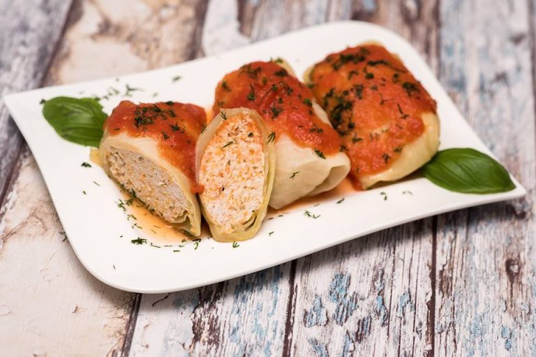 Three cabbage rolls in tomato sauce with dill on a white plate