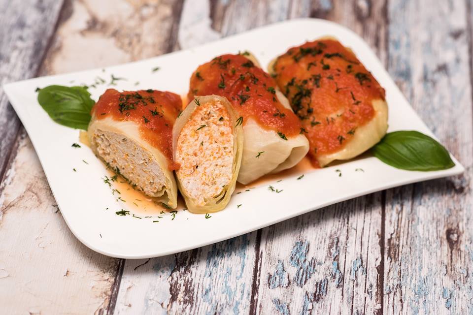 Three cabbage rolls in tomato sauce with dill on a white plate, one cut open