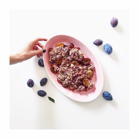 Baked oat porridge with plums and crumble in a pink oval dish, whole plums around it