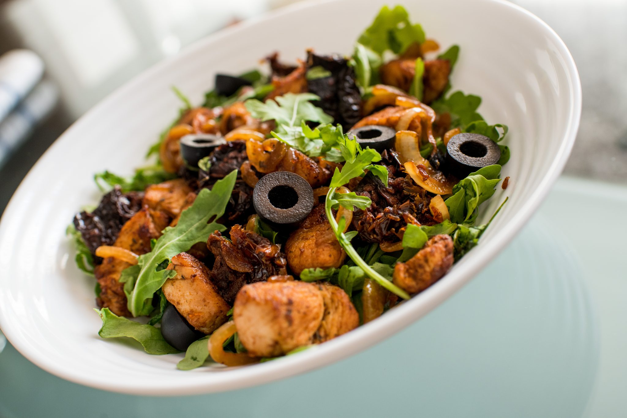 Turkey salad with rocket, black olives and dried tomatoes in a white bowl