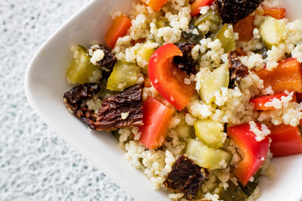 Millet salad with red pepper, pickled cucumber and dried tomatoes in a white dish