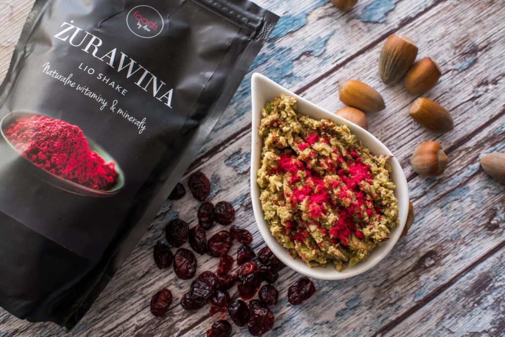 Avocado cream sprinkled with cranberry powder in a white bowl, with dried cranberries and hazelnuts