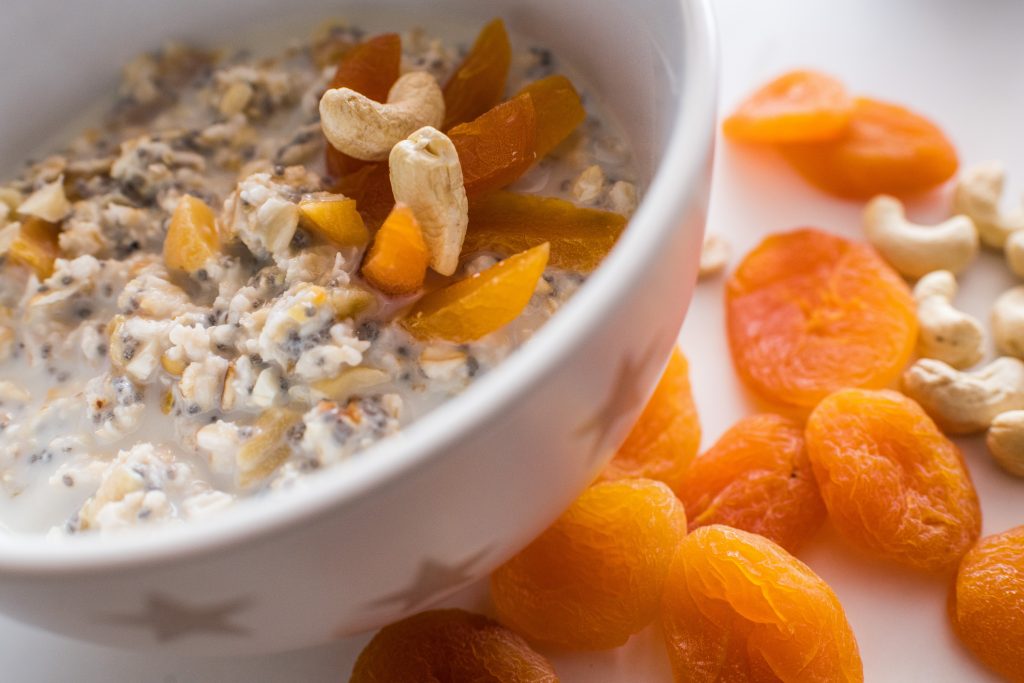 Oats with chia seeds topped with cashew nuts and dried apricots, with more apricots beside the bowl