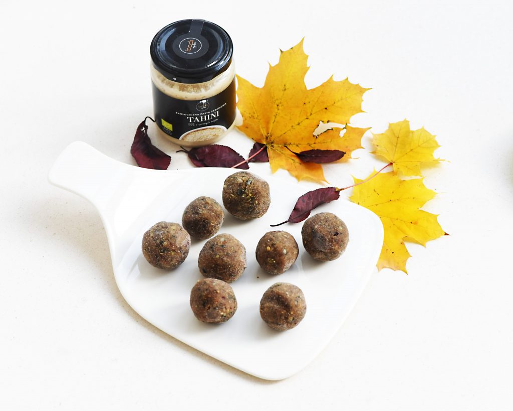 Power balls on a white board with a jar of tahini and autumn leaves