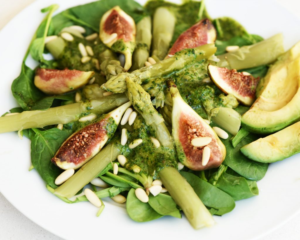 Salad of asparagus, figs and baby spinach with green sauce, pine nuts and avocado on a white plate