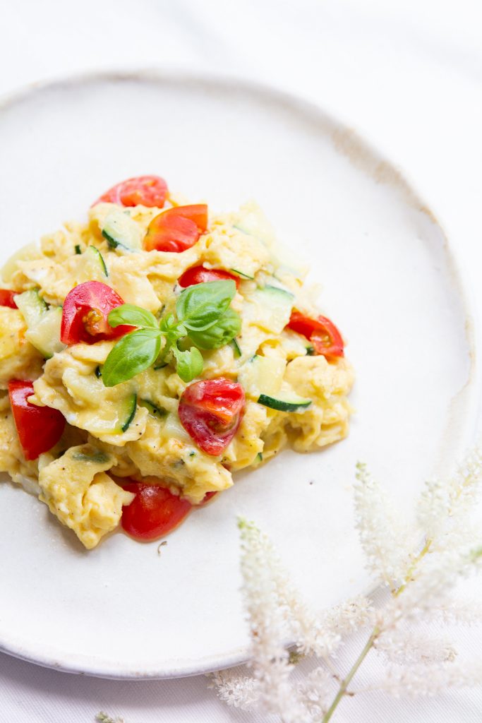 Scrambled eggs with tomatoes and basil on a white plate