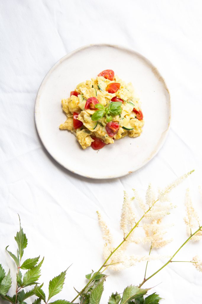 Plate of scrambled eggs with tomato pieces, seen from above on a white cloth