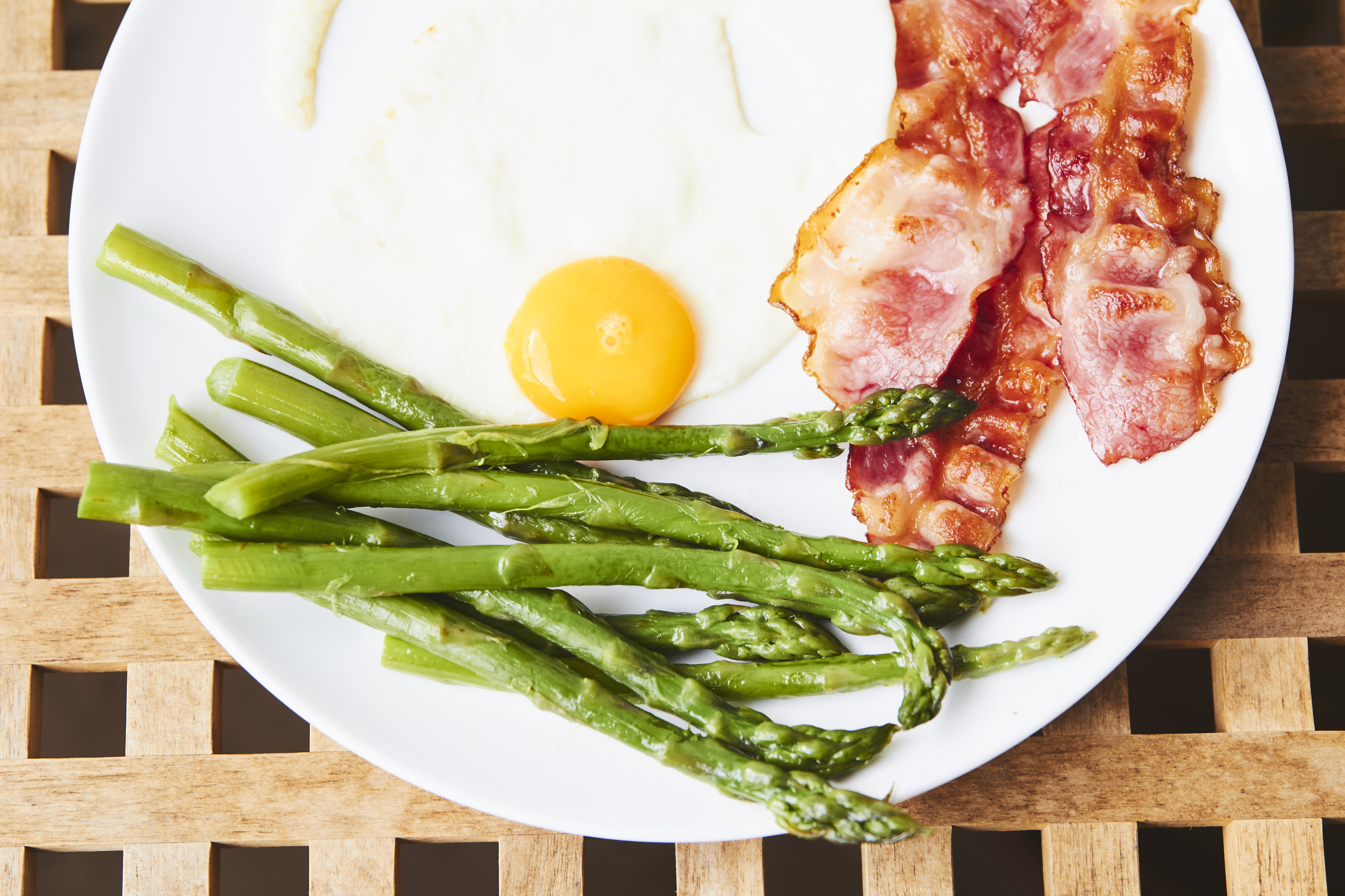 A fried egg, rashers of bacon and roasted asparagus on a white plate, seen from above
