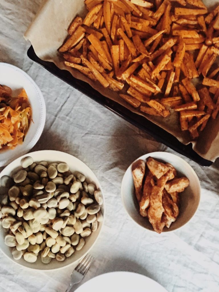 Tray of baked sweet potato strips with bowls of broad beans and chicken
