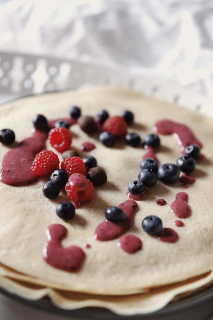 Close-up of thin pancakes topped with berry sauce, fresh blueberries and raspberries