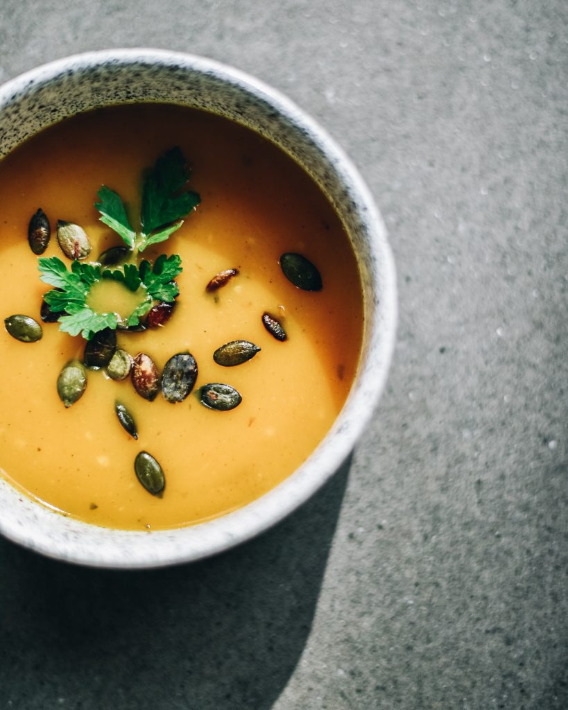 Pumpkin cream soup with pumpkin seeds and parsley in a speckled bowl on a grey surface