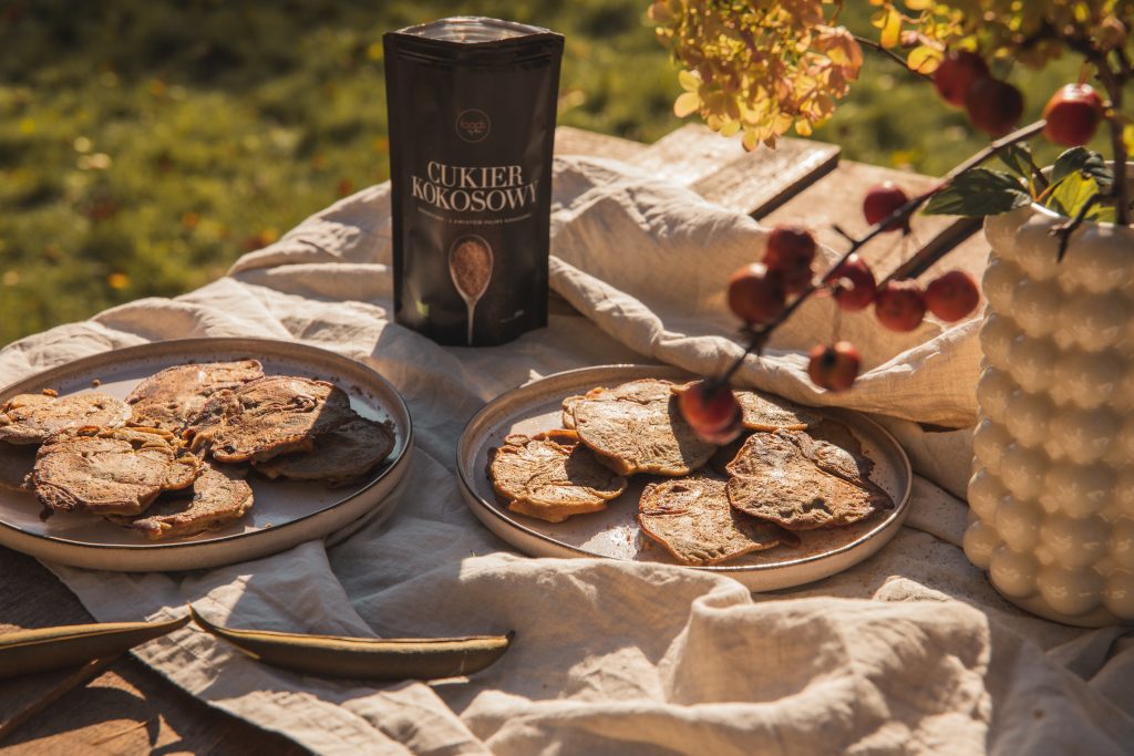 Two plates of apple crumpets outdoors on a linen cloth, with a pack of coconut sugar and autumn branches