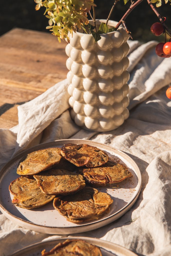 Plate of apple crumpets on a wooden table with a white vase and autumn branches
