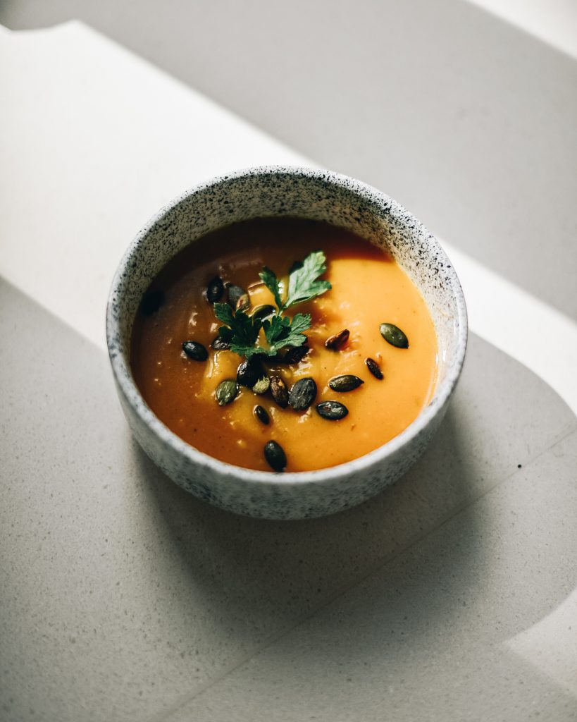 A small bowl of pumpkin cream soup with seeds and parsley in strong sunlight