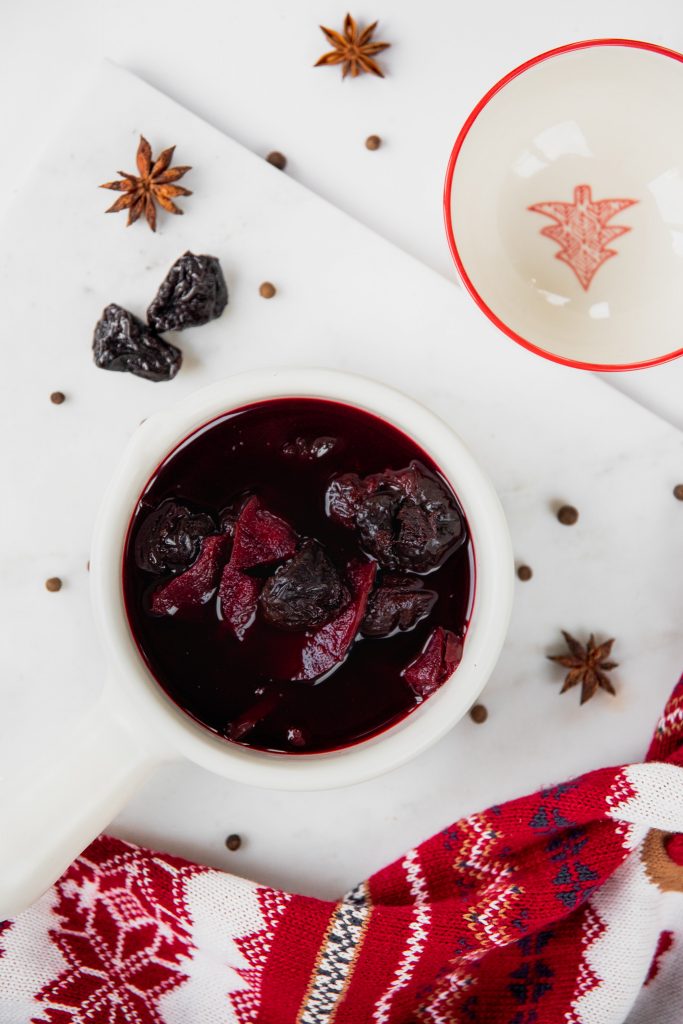 Bowl of deep red borscht with pieces of dried fruit, on a marble board with star anise and a Christmas cloth