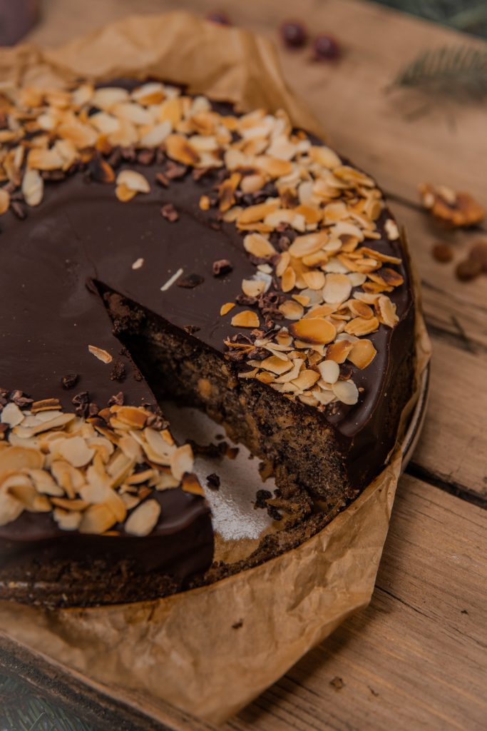 Close-up of a poppy seed cake with chocolate glaze and flaked almonds, showing the dark poppy seed crumb