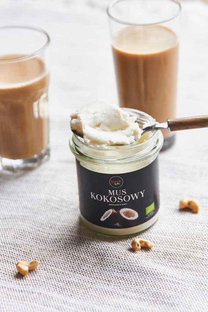 Two glasses of coffee with a jar of coconut spread and a spoon on a linen cloth