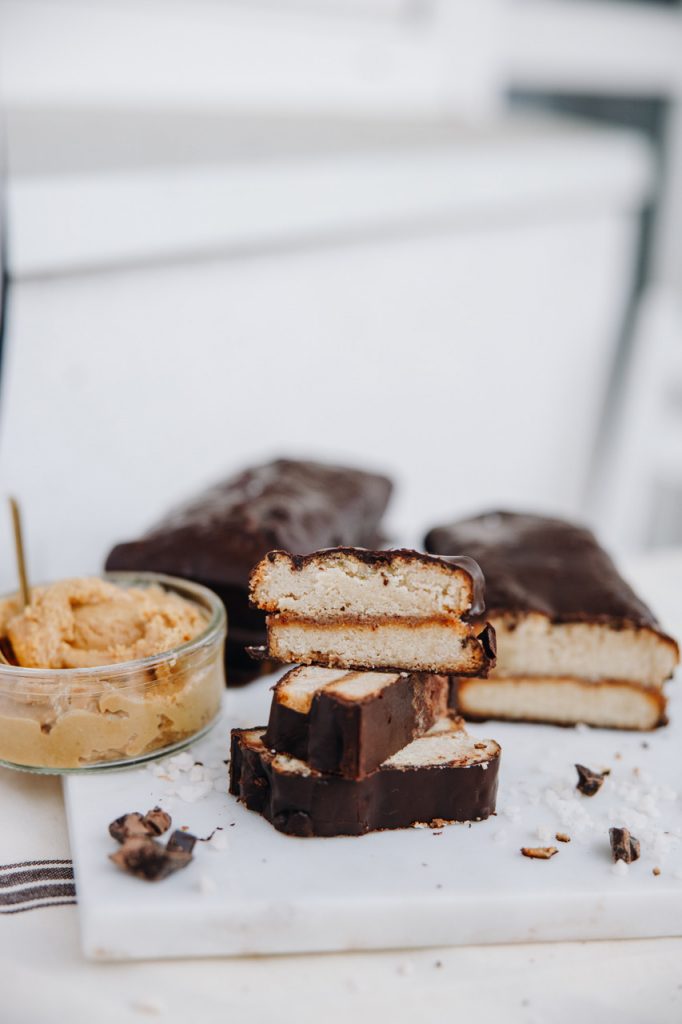 Sliced homemade twix bars showing the shortcrust, caramel and chocolate layers, with a jar of nut butter