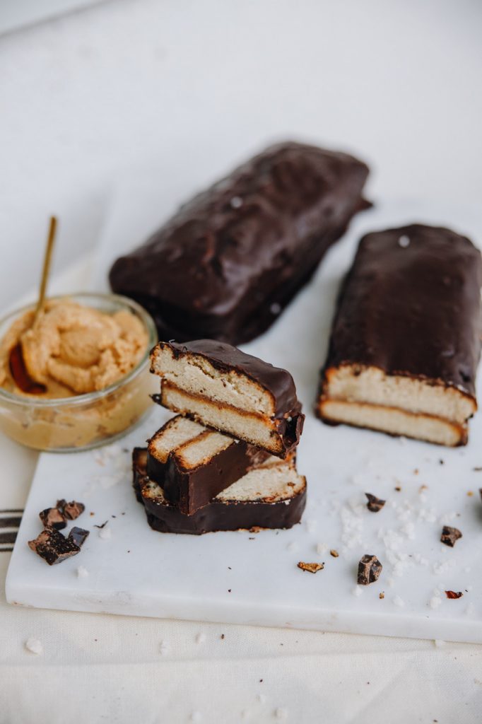 A whole chocolate-covered twix loaf beside cut slices and a jar of caramel