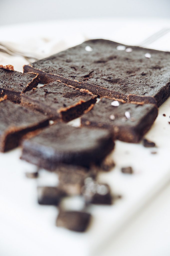 Close-up of cut brownie squares showing the dense, fudgy crumb, with pieces of dark chocolate beside them