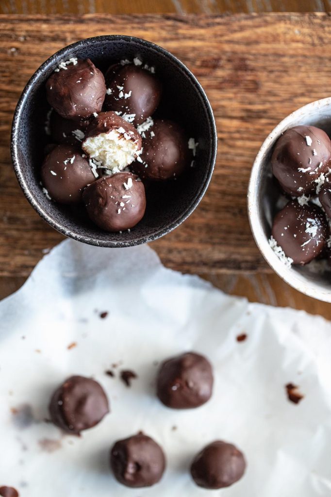 Bounty balls in a bowl, one broken open to show the white coconut filling