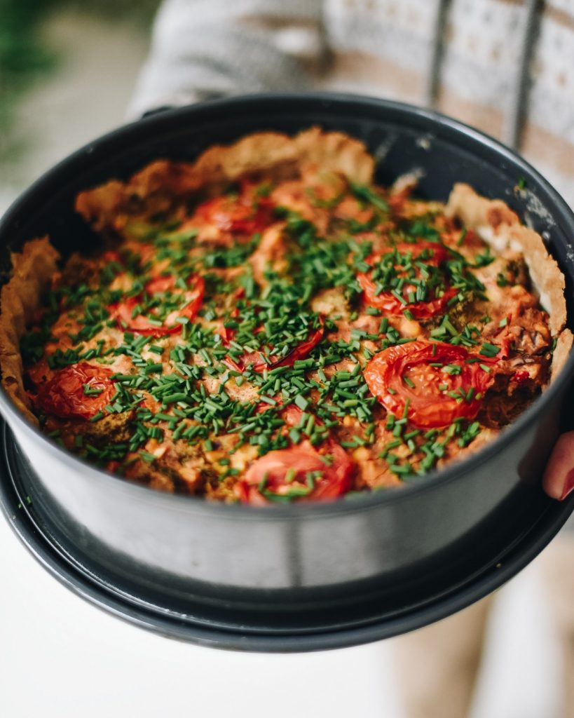 A savoury tofu and vegetable tart topped with tomato slices and chopped chives in a springform tin