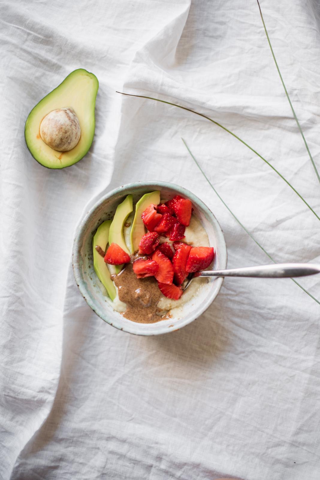 Millet porridge with avocado slices, chopped strawberries and almond spread in a ceramic bowl, seen from above