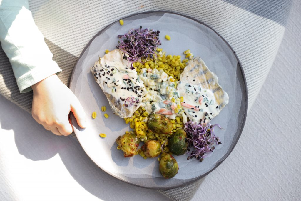 Baked zander with sauce, turmeric pot barley and Brussels sprouts on a grey plate
