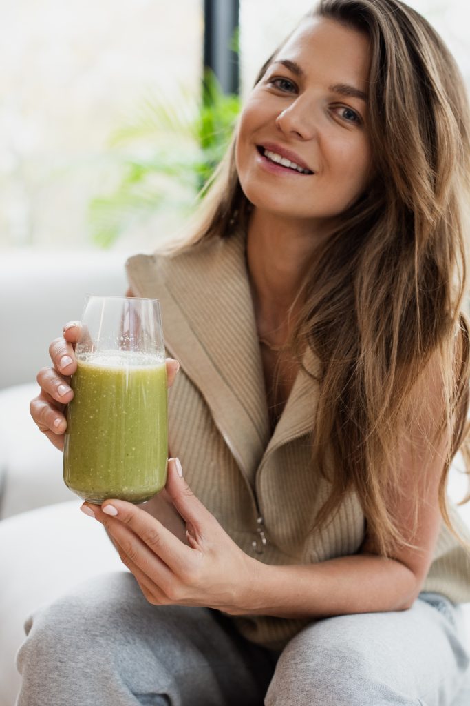 Anna Lewandowska holding a glass of green smoothie while sitting on a light sofa