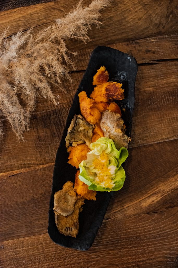 Sweet potato mash with breaded oyster mushrooms and lettuce on a dark slate board