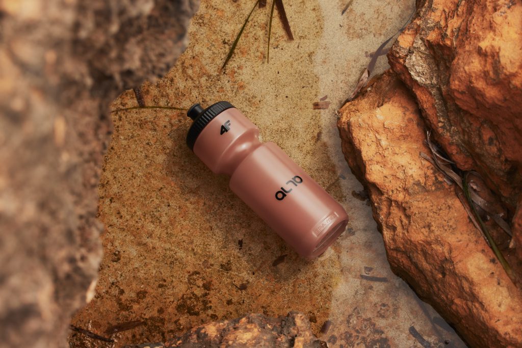 A pink reusable water bottle lying on a rock