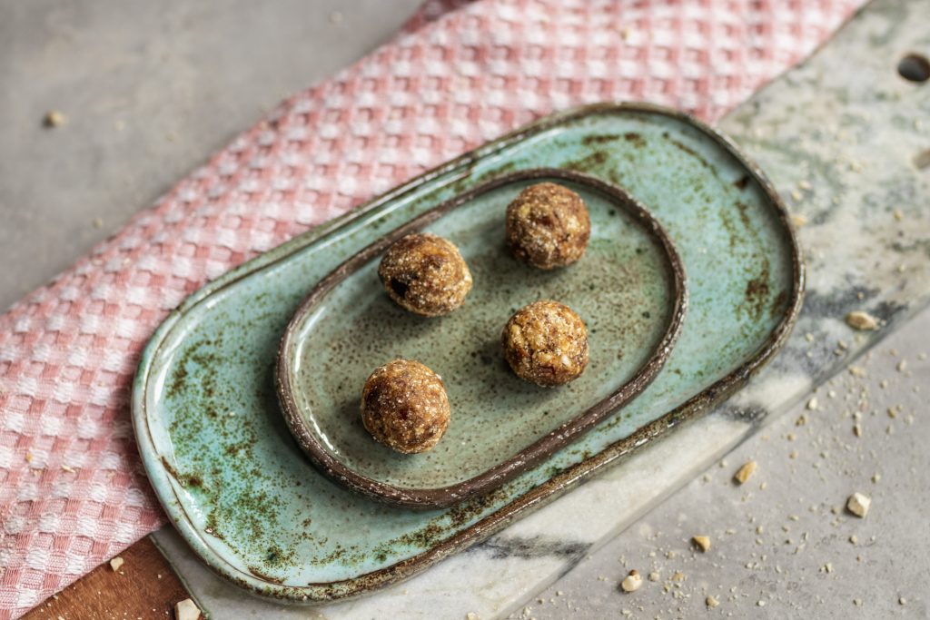 Three date energy balls on a green ceramic dish on a pink cloth