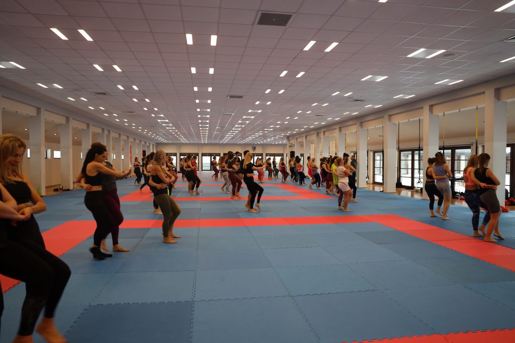 A large hall with people dancing in pairs on red and blue mats during a workshop