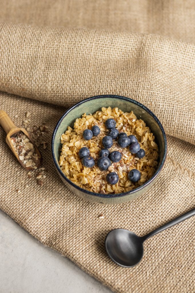 Oat porridge with blueberries and chopped almonds in a green ceramic bowl on hessian cloth