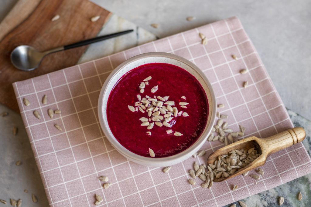 Bowl of deep pink raspberry and beetroot cold soup topped with sunflower seeds