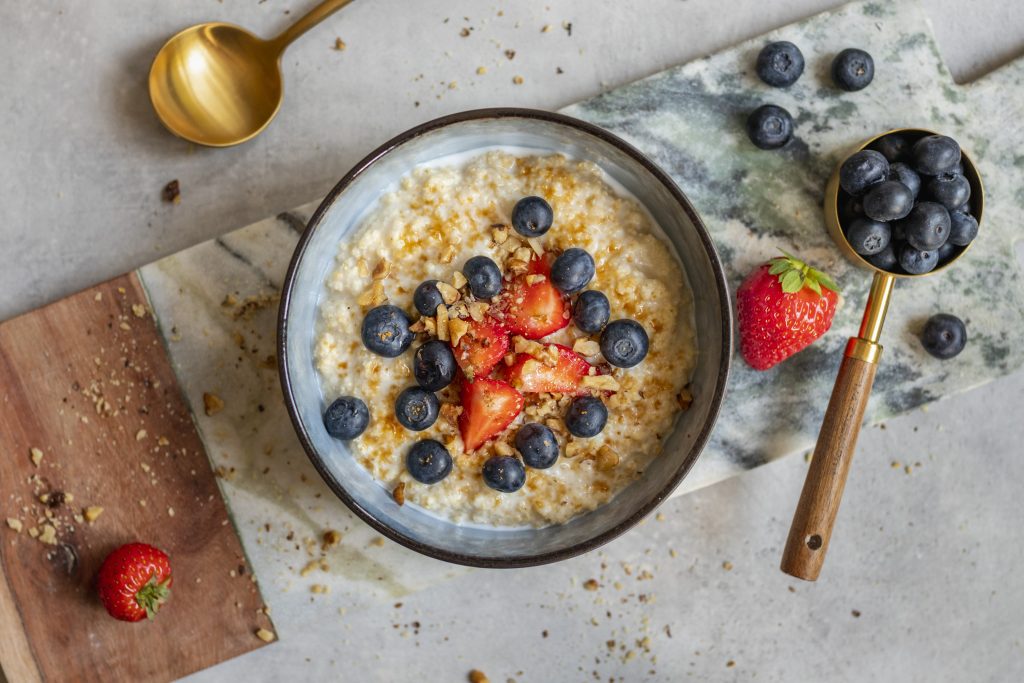 Bowl of millet porridge topped with blueberries and chopped strawberries, with a gold spoon on a marble board